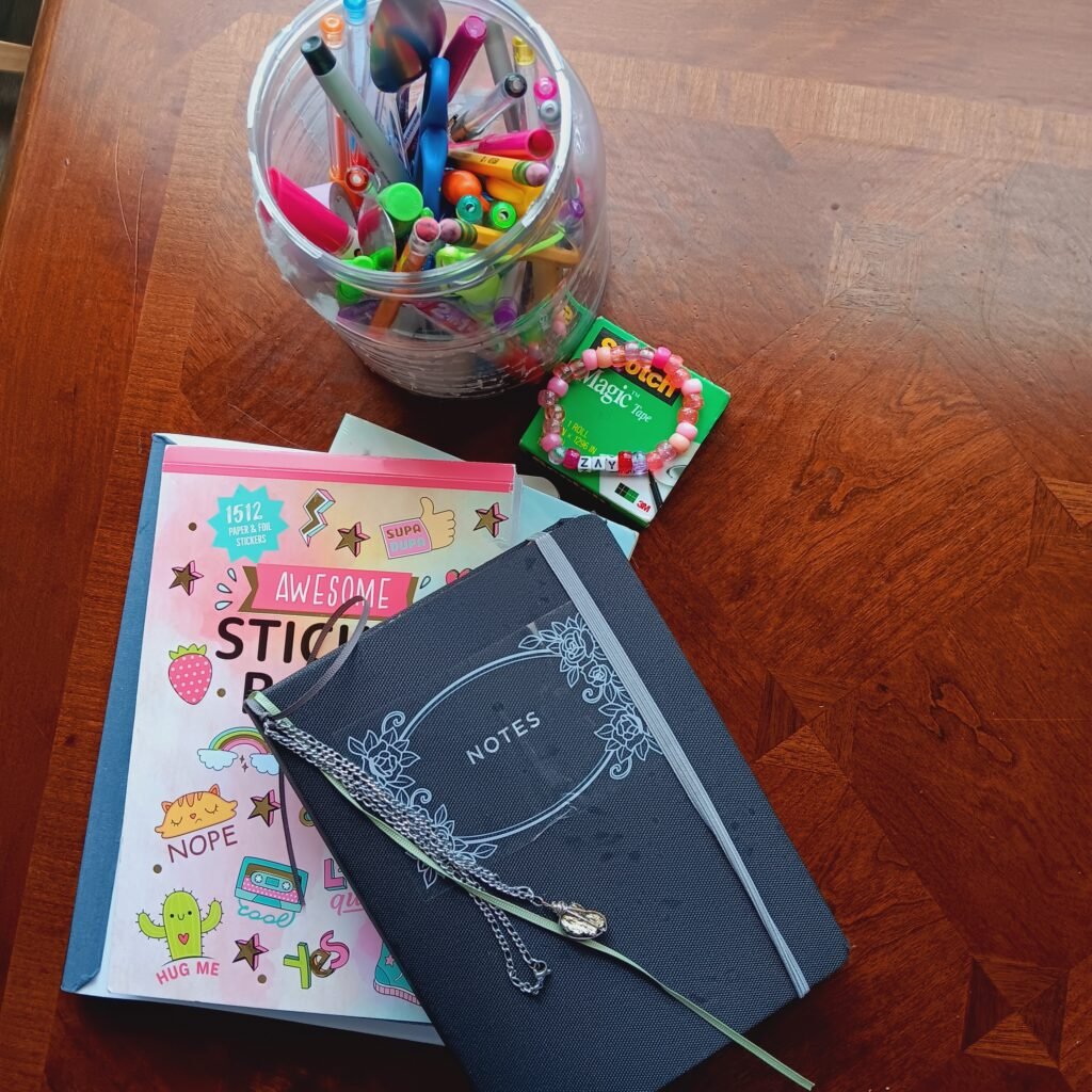 Moodboard creativo con materiales de journaling, cuaderno negro, stickers y marcadores sobre mesa de madera